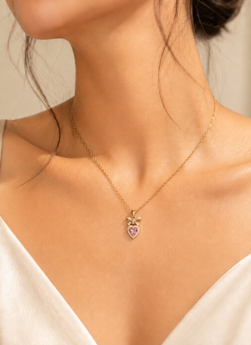 Pink Crystal Heart Necklace featuring a sparkling heart-cut pink crystal with crystal bow pendant in gold finish